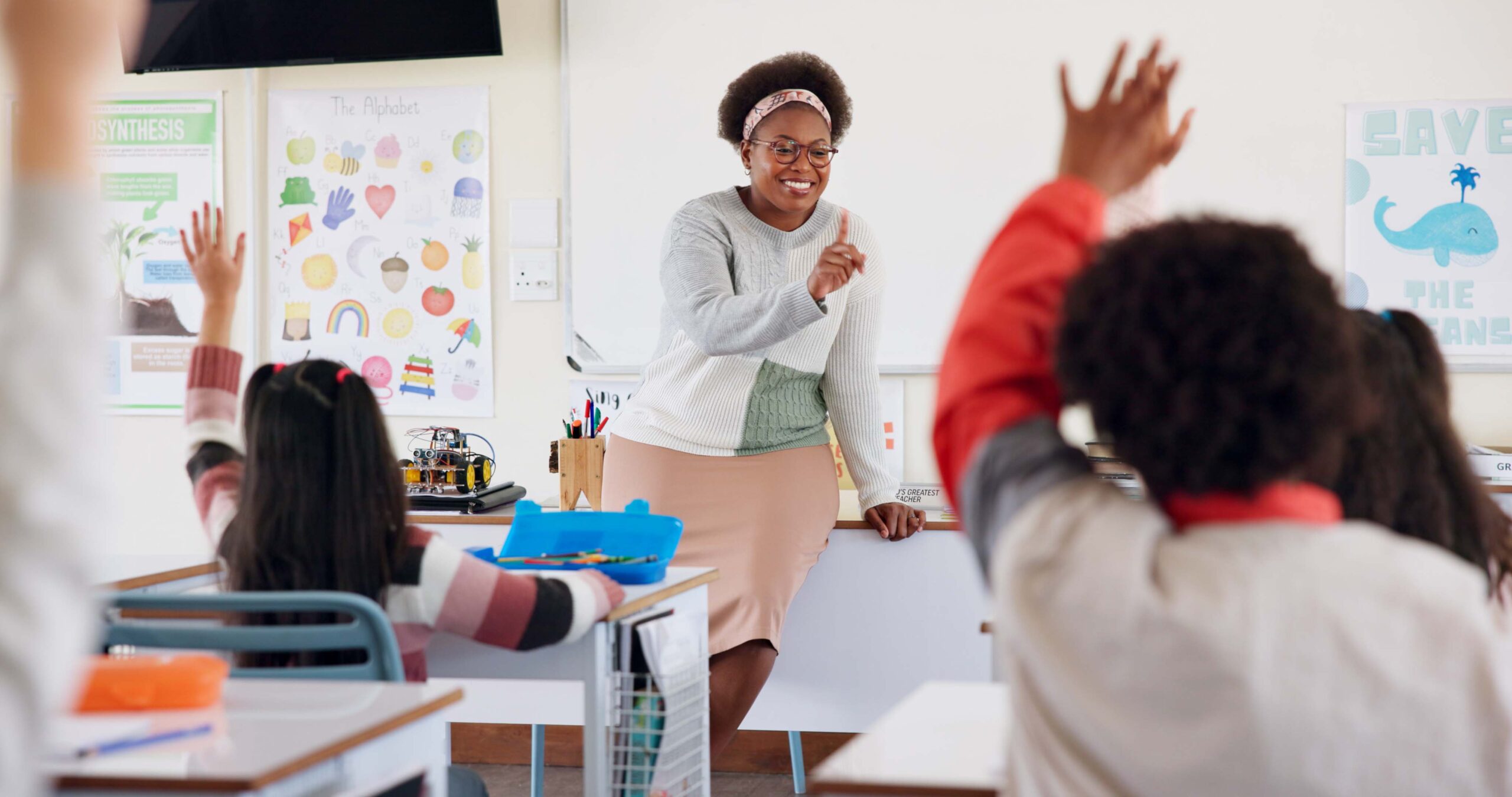 Raised-hand young students and a teacher in a classroom
