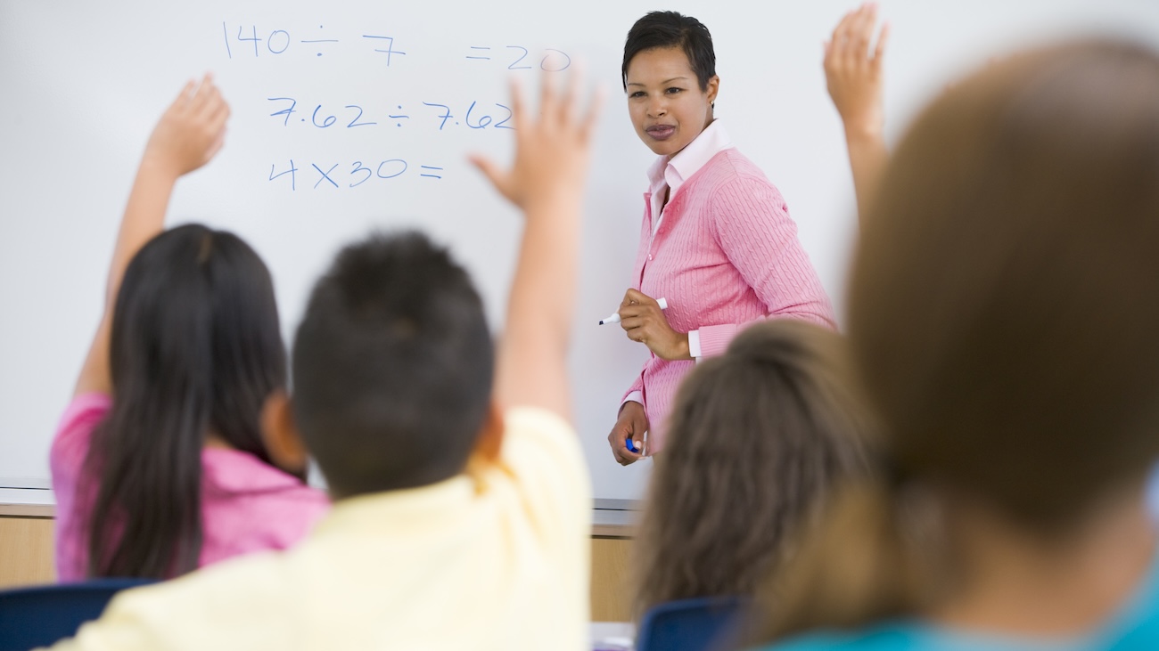 female teacher at a whiteboard in front of a class of students