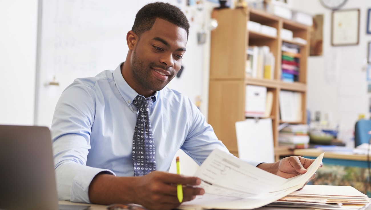 Black male teacher at his desk reviewing papers.