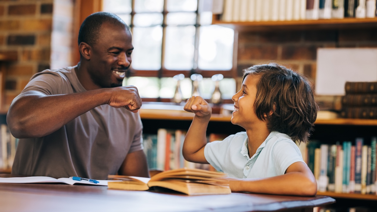 Black male teacher fist bumping a young mixed race male student